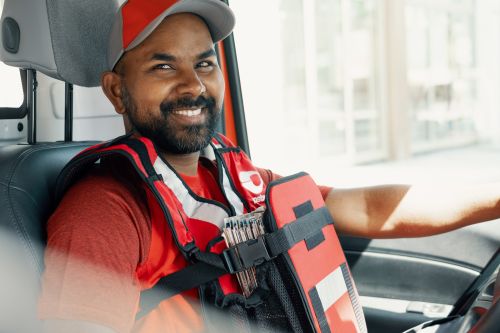 Smilende postbud sitter i førersetet i postbilen sin.